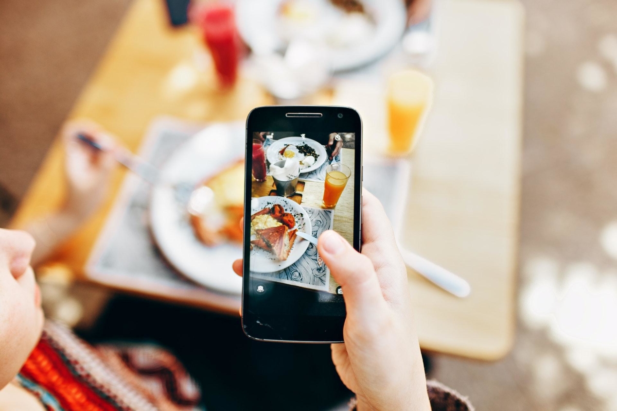Person holding a smartphone taking a photo of a plate of food.